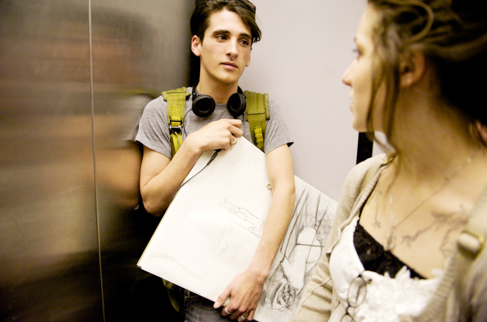 Male student in an elevator wearing headphones, with female student looking back