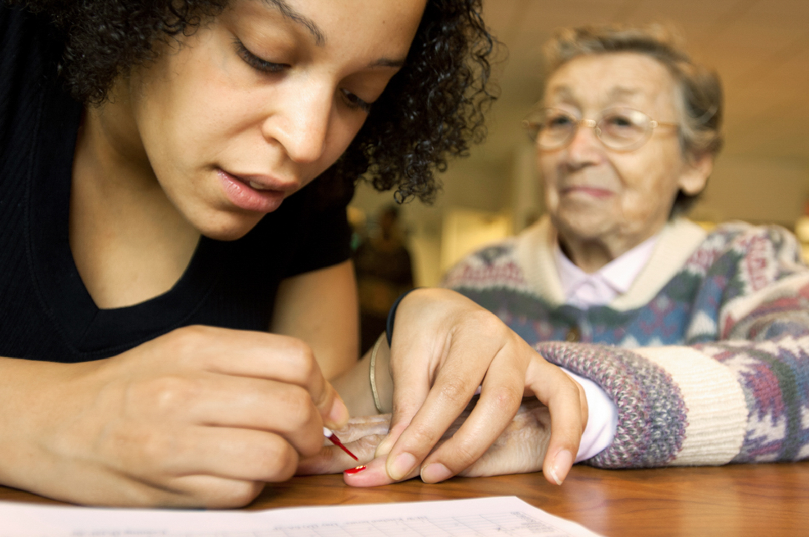 Close up of caretaker applying nail polish on elderly woman