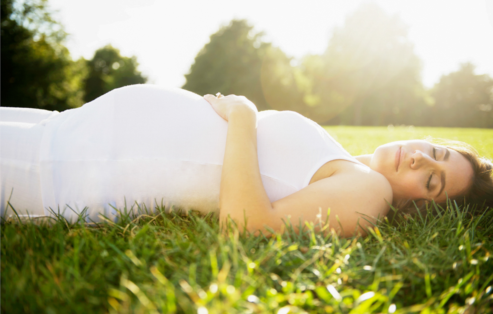 Pregnant woman lying down on grass, with eyes closed 