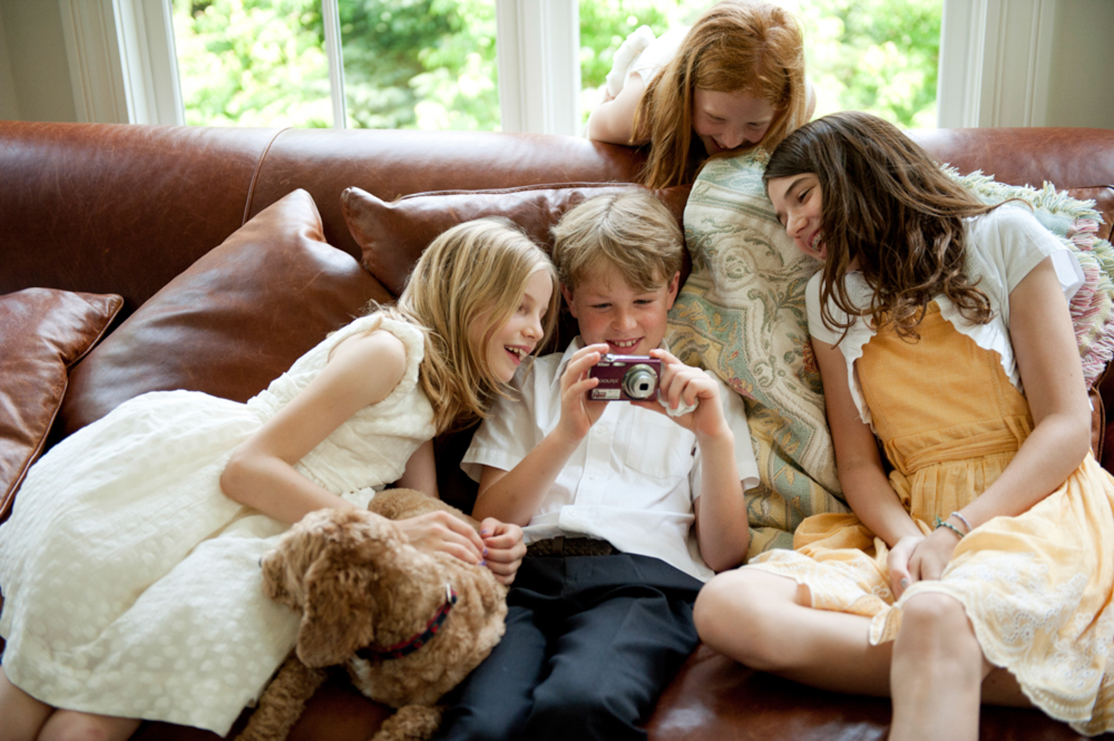 Children sitting on a sofa looking at a camera with a dog