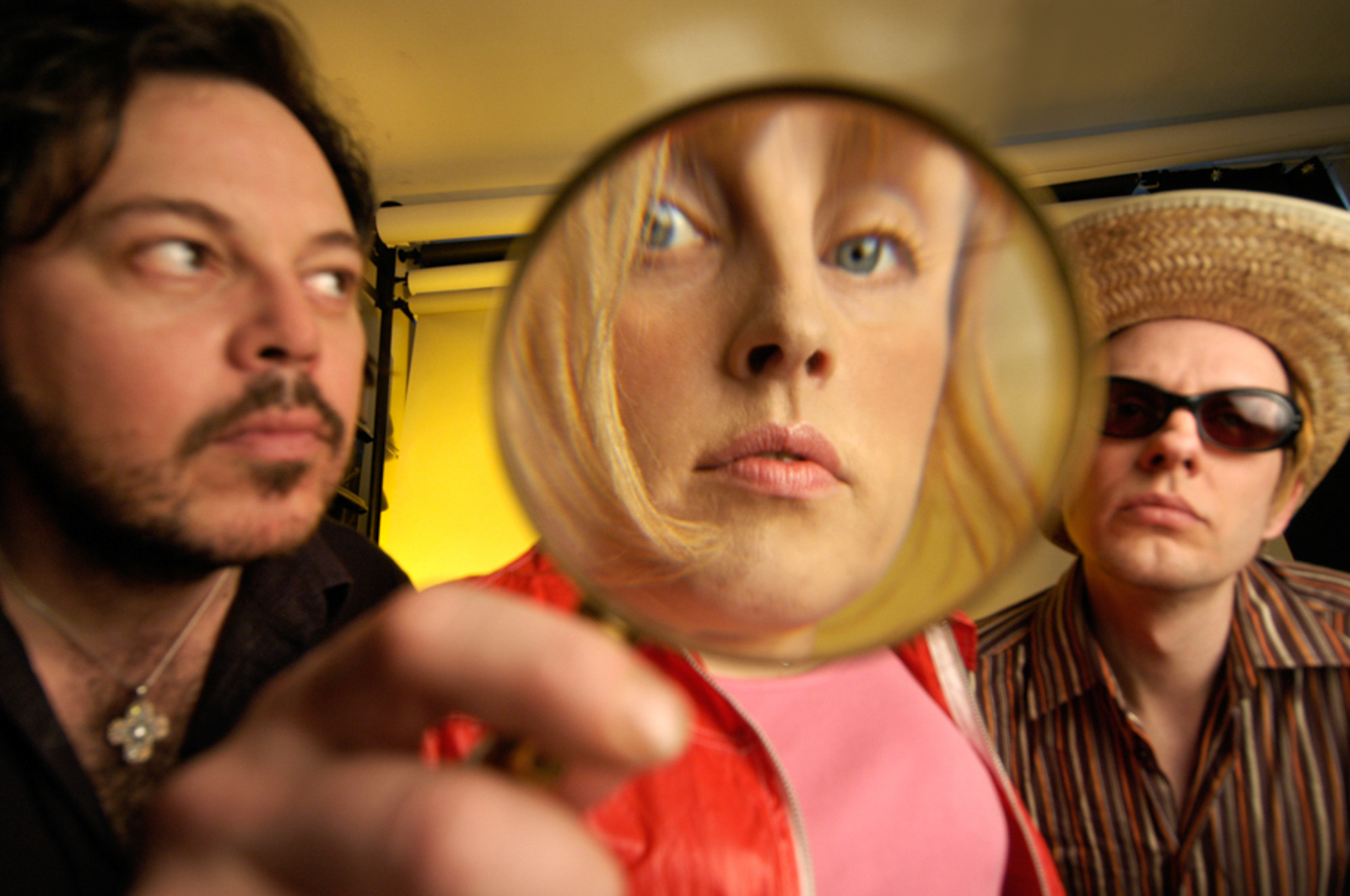 Portrait of band, with a man holding a magnifying glass in front of a woman's face