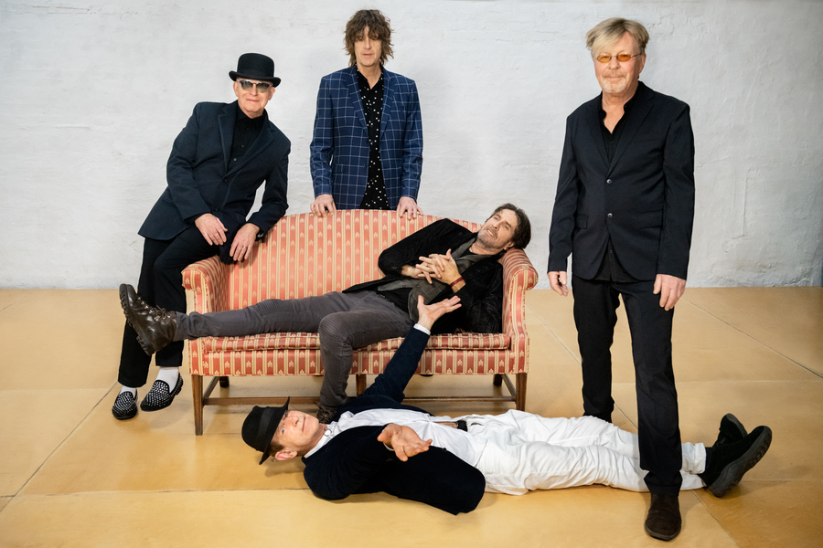 Rock band The Fixx casually lounging in and around a vintage couch, in front of a white background