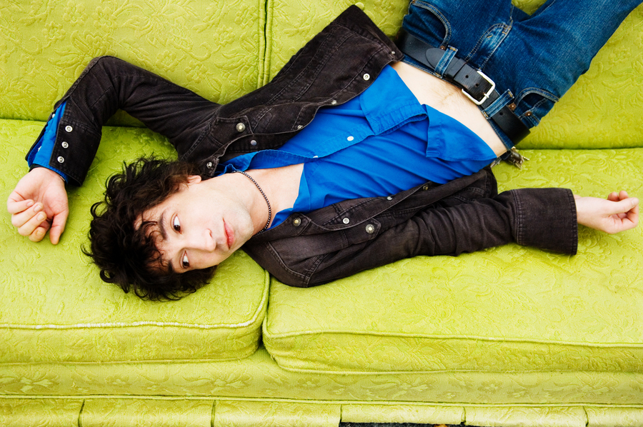 Young man lying upside down on green couch, with a cool demeanor