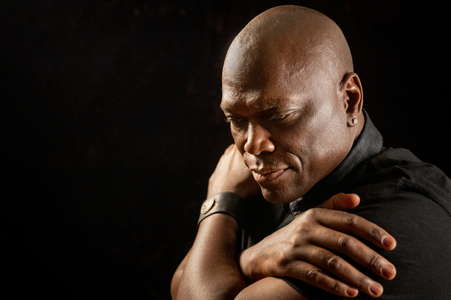 Man with his arms crossed around himself, with a pensive expression, in front of a black background