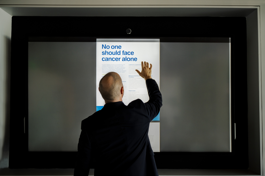 Man standing in front of a touchscreen, facing away from the camera, in a healthcare setting