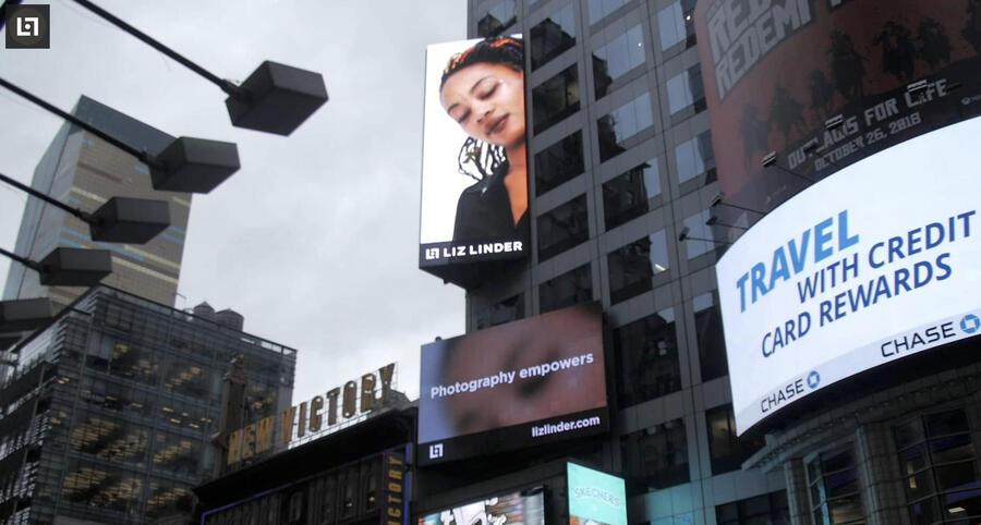 Times Square lit billboards featuring a  photo of a woman and the liz linder logo beneat it.