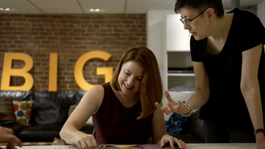 two business woman at a desk with the word BIG behind them