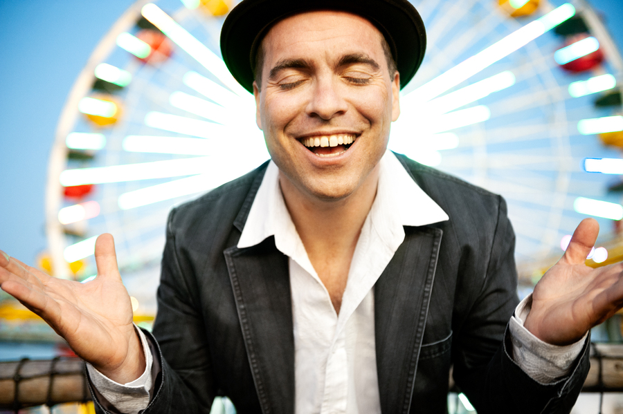 Man standing in front of a ferris wheel with his arms open, eyes closed and a placid smile