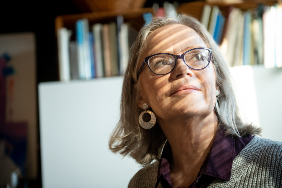 Woman inside a study, looking out a window with a pensive expression as light washes over