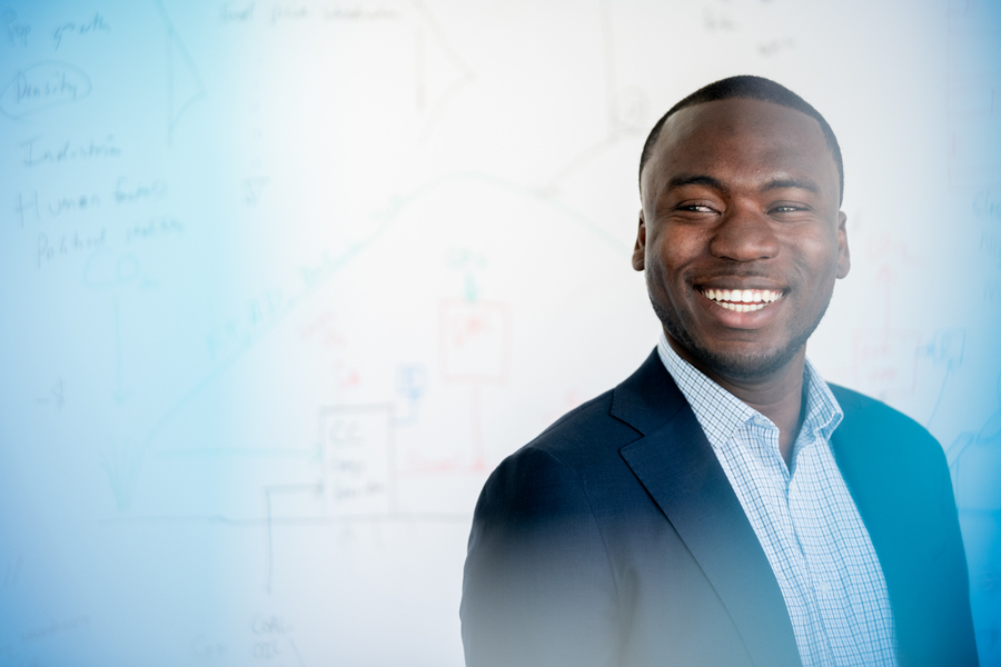 Man standing in front of whiteboard, in an academic setting, with a warm smile 