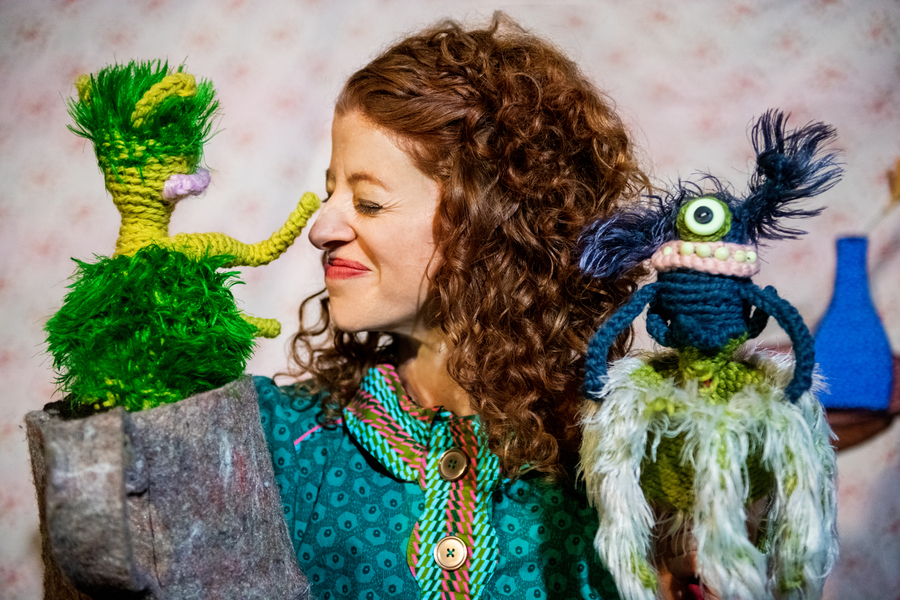 Female puppeteer holding two puppets, playfully scrunching her nose towards them