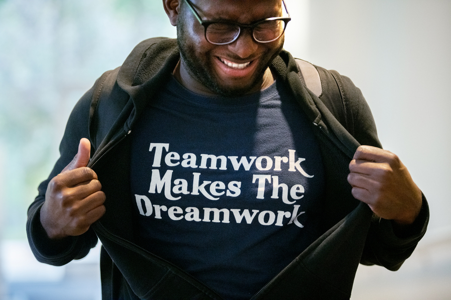 Man wearing glasses, opening his sweater to reveal a t-shirt with an inspirational quote