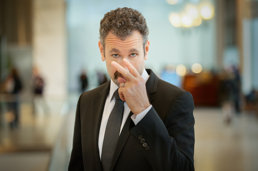 Man in a suit pointing at his eyes, in a commercial environment