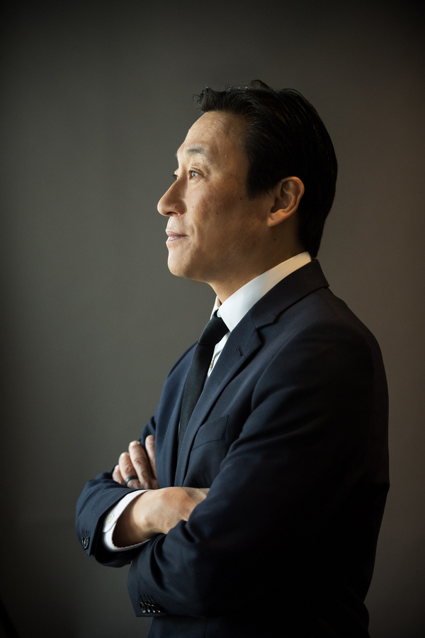 Side profile of a man with a soft smile, looking upwards, in a plain background