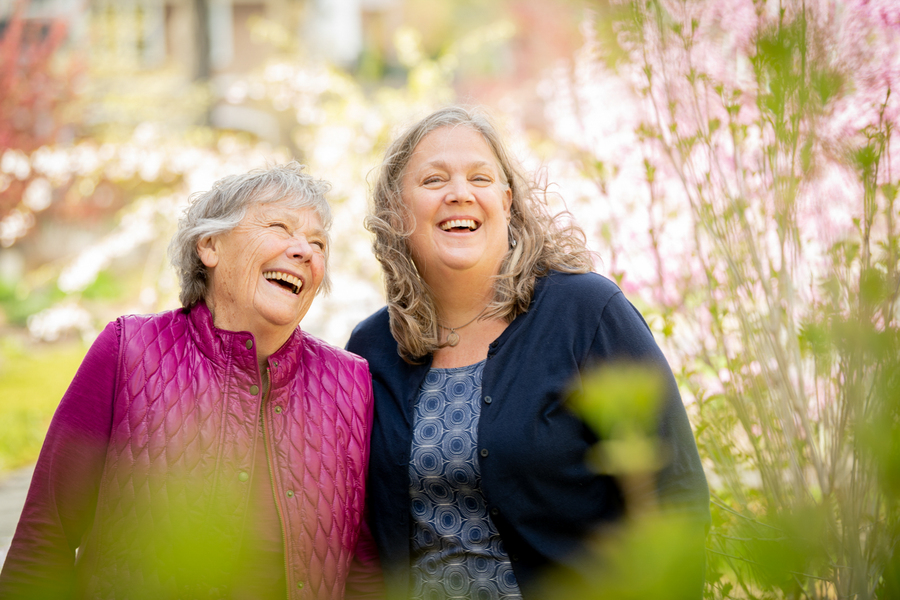 Two older women smiling, standing in a garden outdoors