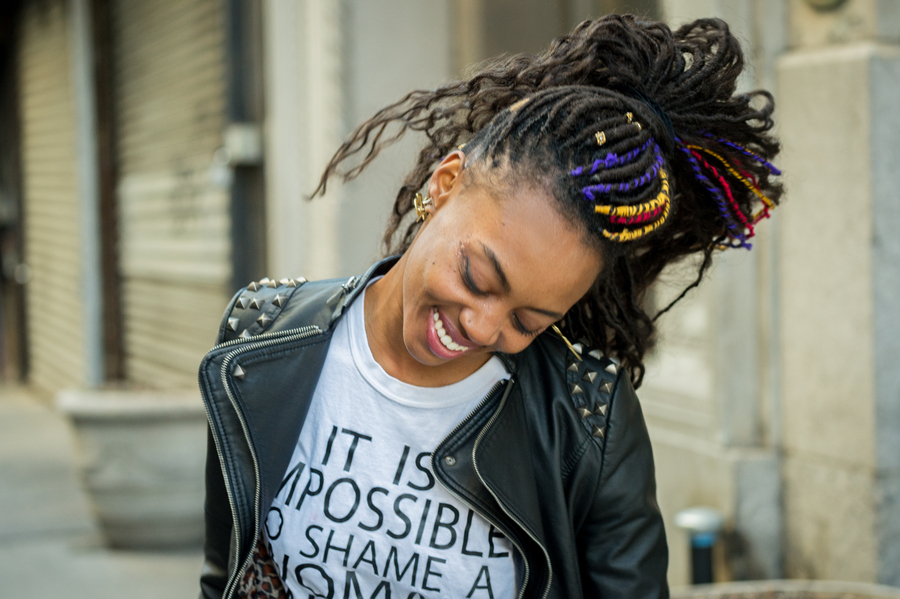 Woman with colorful dreads in motion on a sidewalk, with a cheerful smile